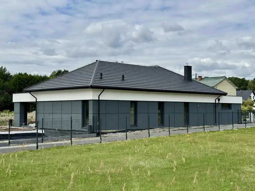 Elewacja boczna z oknami w ciemnych ramach, widok przez łąkę zza ogrodzenia, Homekoncept 70, Leżajsk