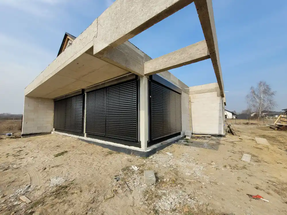Narożnik z żaluzjami fasadowymi pod wysuniętym stropem i betonową belką, Homekoncept 79, Warszawa